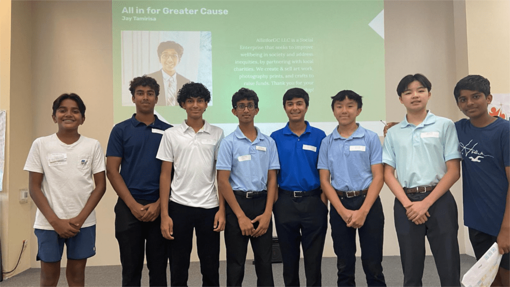 Eight young individuals stand in a group indoors, smiling at the camera. A presentation slide with text and an image of a person is projected behind them on the wall.